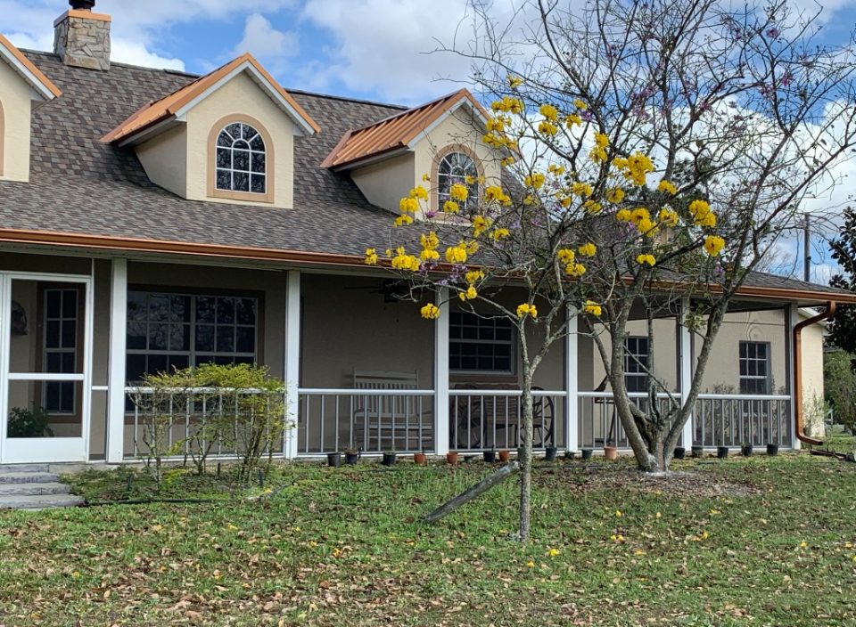 Shingle roof with copper-colored metal dormer roofs and gutters on a home with a wraparound porch